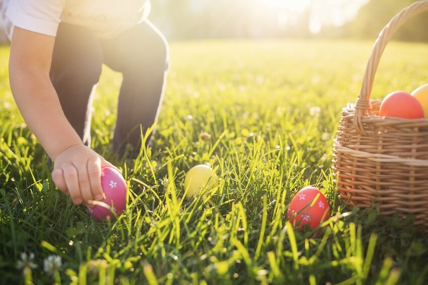 Easter egg hunt ideas: kid picking up colorful Easter eggs from the grass beside a basket